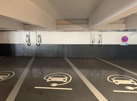 Places de stationnement réservées aux véhicules électriques avec bornes de recharge murales et marquage au sol.