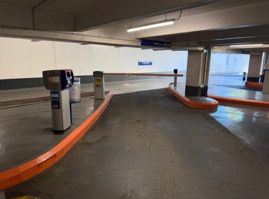 Voie d'accès vers la barrière de sortie avec borne Skidata et signalétique « À bientôt » en fond.