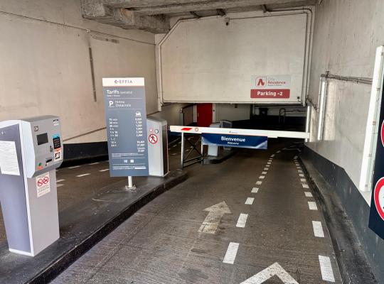 Borne de ticket avec barrière levante et panneau des tarifs à l'entrée de la rampe du parking Delacroix.