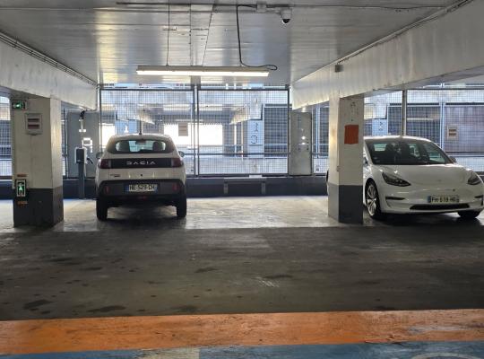 Emplacements de stationnement intérieurs occupés par deux véhicules face à une structure métallique ajourée.