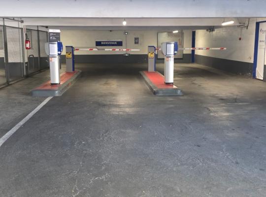 Double voie d'accès intérieure avec bornes de distribution de tickets et barrières levantes sous le panneau « Bienvenue ».