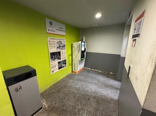 Borne de paiement automatique EFFIA installée près d'un panneau d'information historique sur un mur vert.