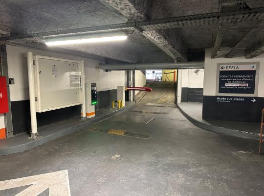 Voie d'accès couverte du parking avec borne de contrôle à ticket, barrière levante et panneau d'affichage EFFIA.