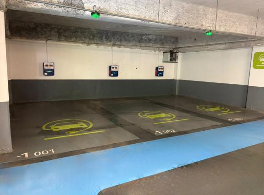 Emplacements de stationnement réservés à la recharge des véhicules électriques avec bornes murales et témoins lumineux verts.