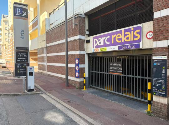 Entrée du Parc Relais Les Arts avec grille automatique, enseigne lumineuse violette et totem d'information des horaires et tarifs.