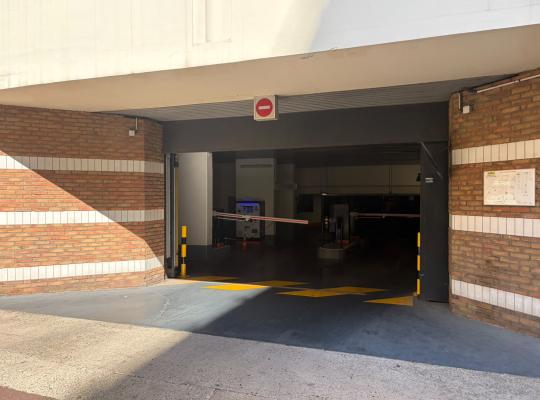 Accès voiture du parking sous un bâtiment en brique et béton, équipé d'un panneau sens interdit et de barrières levantes.