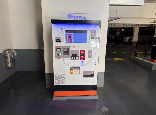 Caisse automatique de paiement EFFIA avec écran tactile et lecteur de cartes, installée près de la voie de circulation.