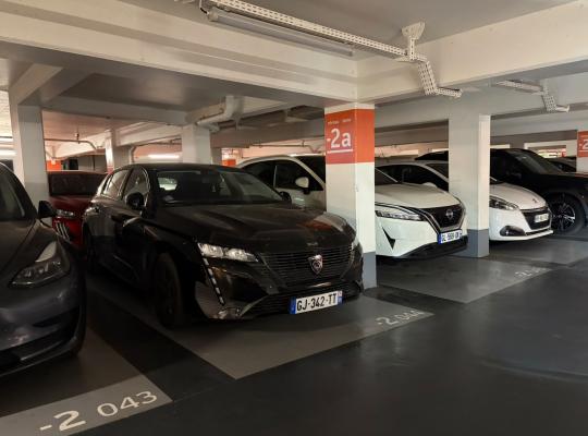 Emplacements numérotés au niveau -2a d'un parking couvert, occupés par plusieurs voitures alignées le long des piliers.
