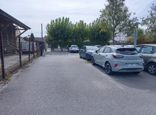 Allée de circulation bordée de véhicules garés dans un parking extérieur.