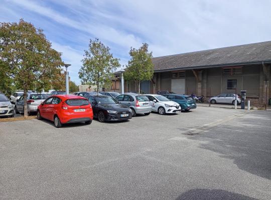 Rangée de voitures stationnées sur le parking devant un long bâtiment.