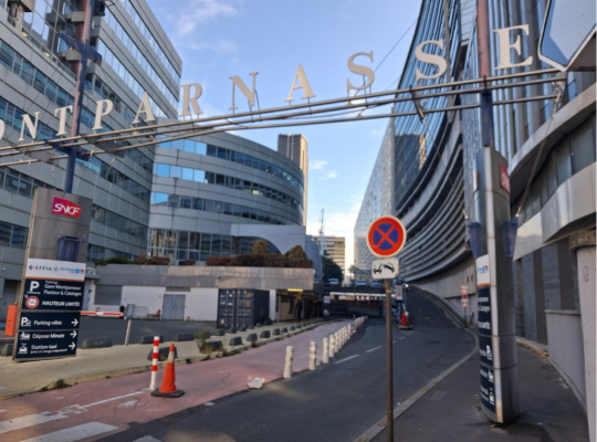 Vue extérieure menant à l'entrée du parking Gare Montparnasse (Pasteur & Catalogne), avec des panneaux indiquant les directions pour le parking vélos, le dépose-minute et la station-taxi.