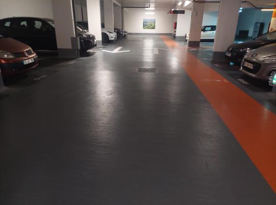 Allée de circulation intérieure d'un parking couvert bordée de voitures.