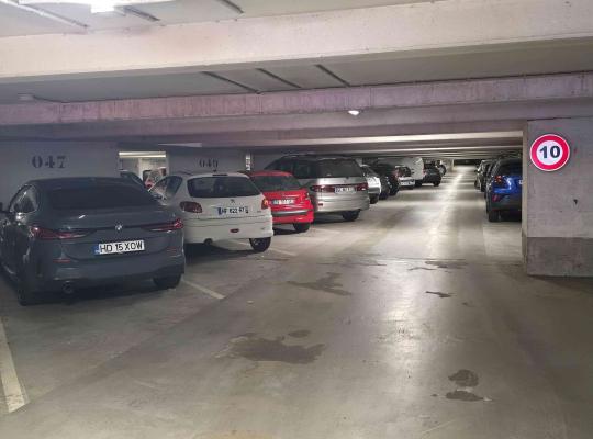 Allée de circulation intérieure d'un parking couvert bordée de voitures.
