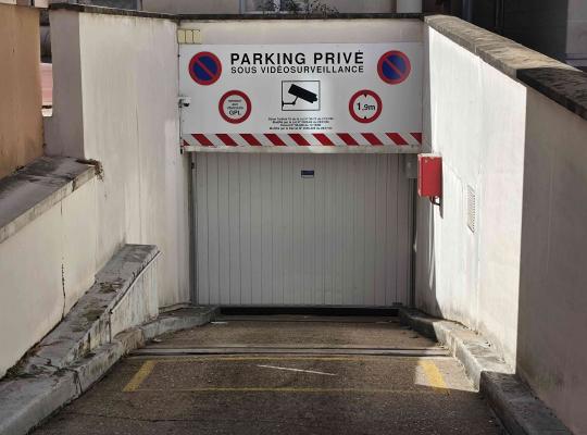Rampa d'accès à un parking privé sous vidéosurveillance avec porte fermée.