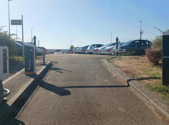 Voie d'accès au parking abonnés premium avec barrière et borne de passage.