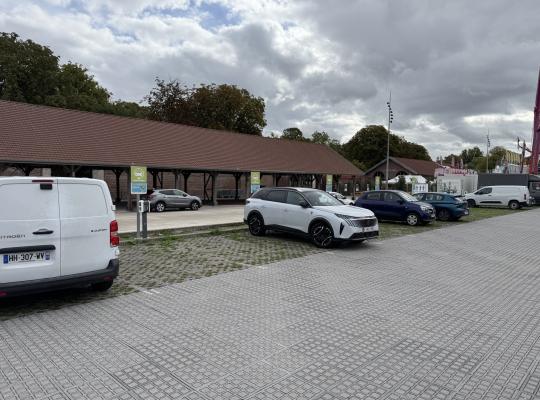 Parking extérieur pavé avec véhicules garés et préau en briques.