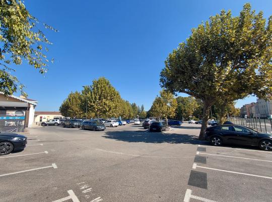Grand parking extérieur arboré avec de nombreuses places de stationnement.