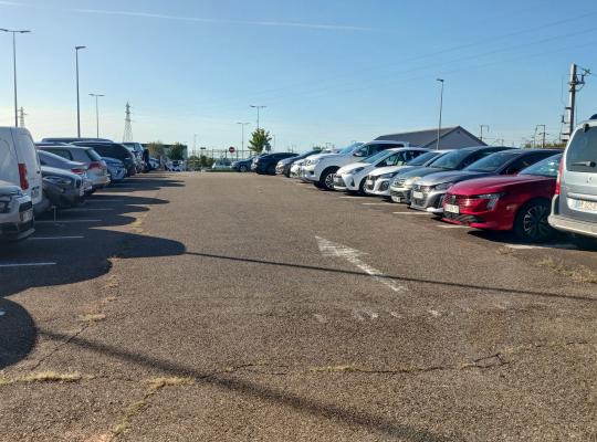 Allée centrale d'un parking extérieur avec de nombreuses voitures stationnées.