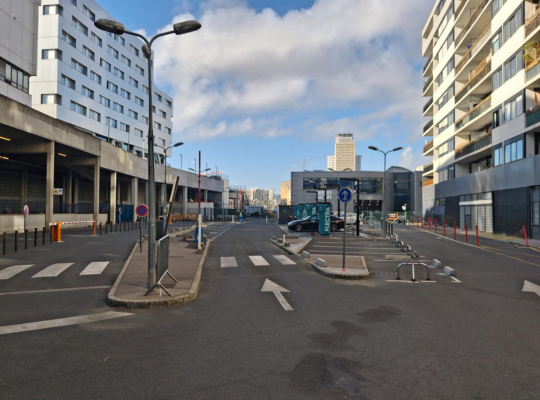 Vue d'une allée urbaine ou d'une rue avec des passages piétons et des bornes de recharge en arrière-plan.