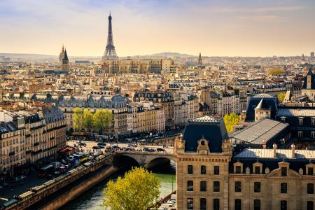 Panorama spectaculaire de Paris au coucher du soleil avec la Tour Eiffel dominant les toits haussmanniens et la Seine: une vue aérienne capturant l'essence de la capitale française, ses ponts historiques et son architecture classique sous une lumière dorée.