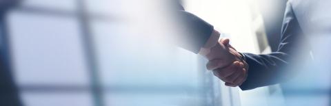 Poignée de main professionnelle entre deux collaborateurs en tenue d'affaires au-dessus d'une table de réunion.