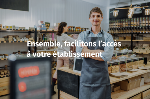 Une photo horizontale en gros plan d'un jeune homme souriant, debout avec les bras croisés, portant un tablier de magasin gris. Il se tient dans une épicerie en vrac bien organisée, avec des étagères remplies de bocaux et de distributeurs de produits secs à l'arrière-plan. Un texte blanc et gras est superposé au centre de l'image, disant : "Ensemble, facilitons l'accès à votre établissement". Une autre personne floue est visible à l'arrière-plan.